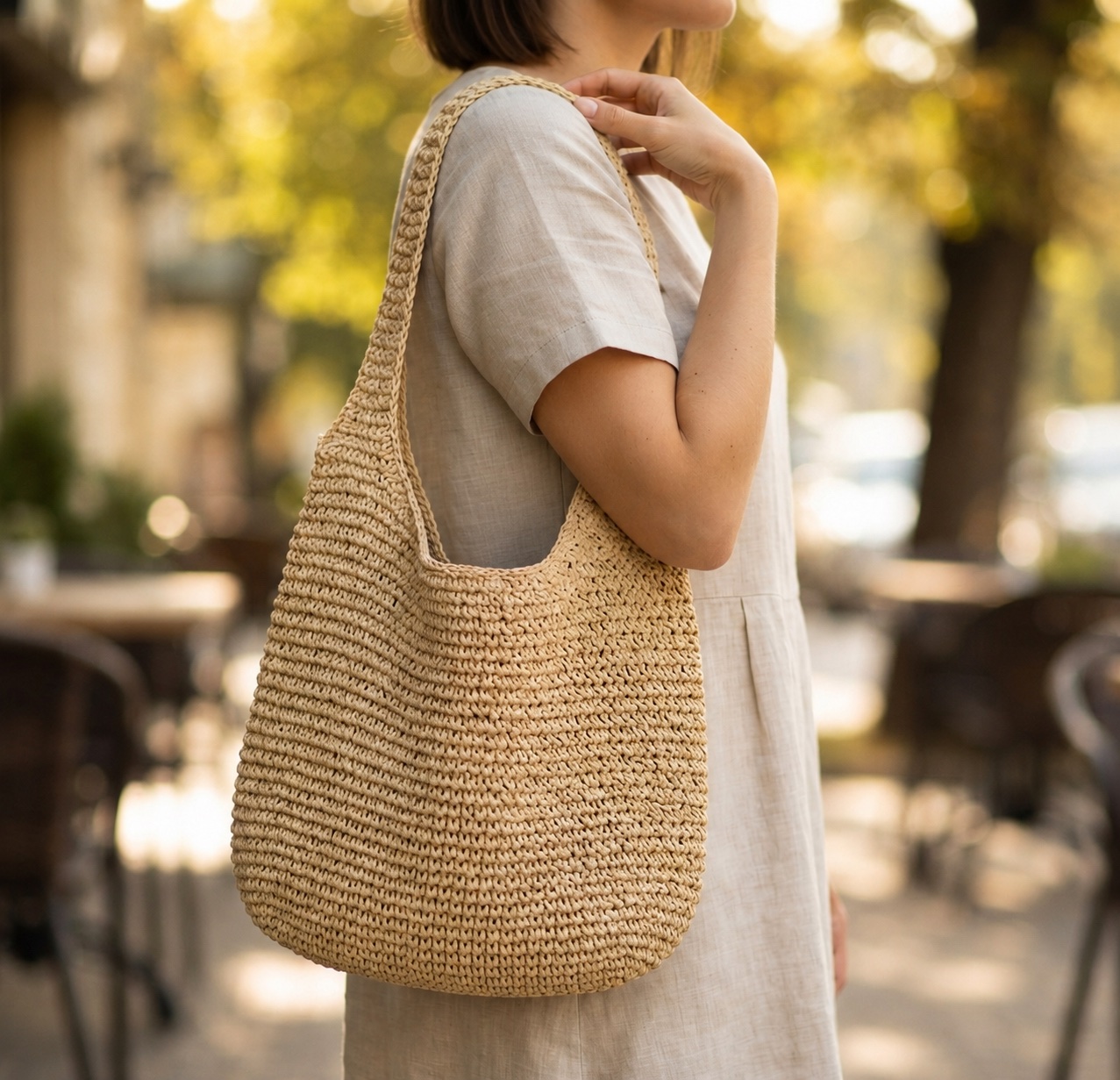 Woman walking a tree-lined city street with the Foldable Straw Tote Bag over her shoulder